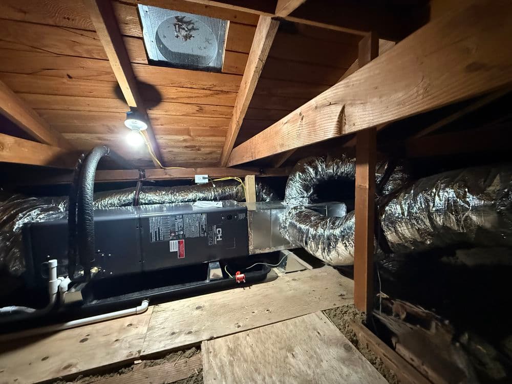 View of ductwork and HVAC system in an attic, showcasing insulation and wooden beams.