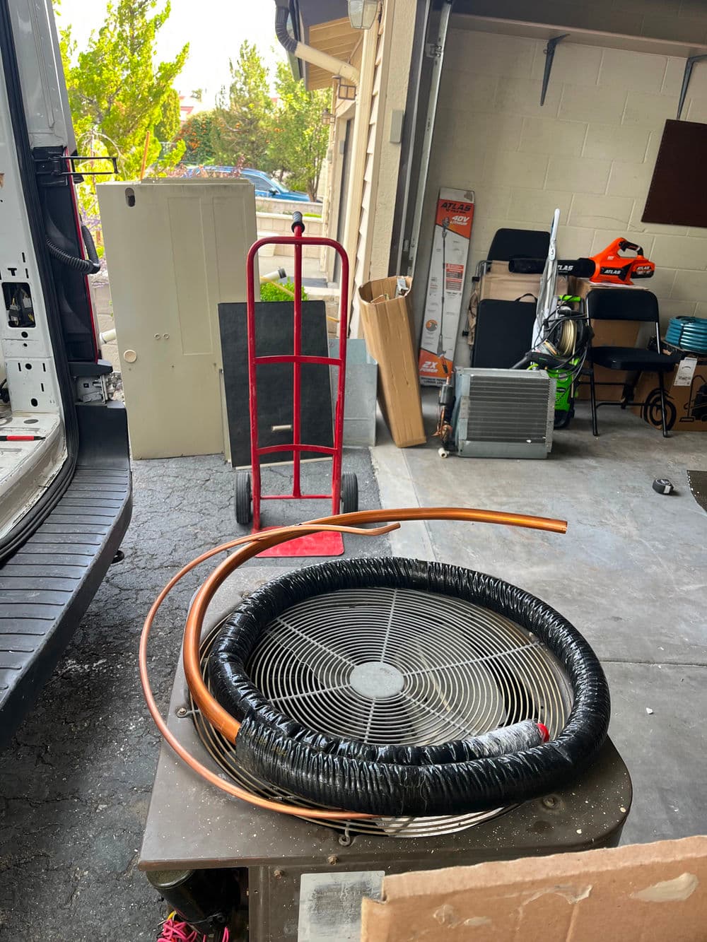 Fan and copper pipes on a table in a garage with moving equipment in the background.