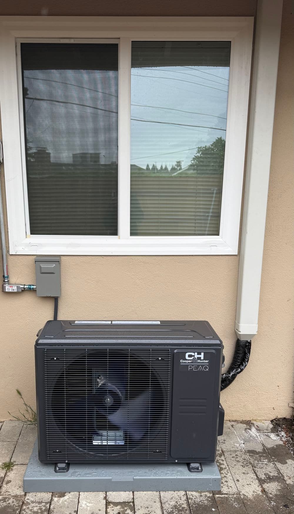 Air conditioning unit installed next to a window on a beige exterior wall.