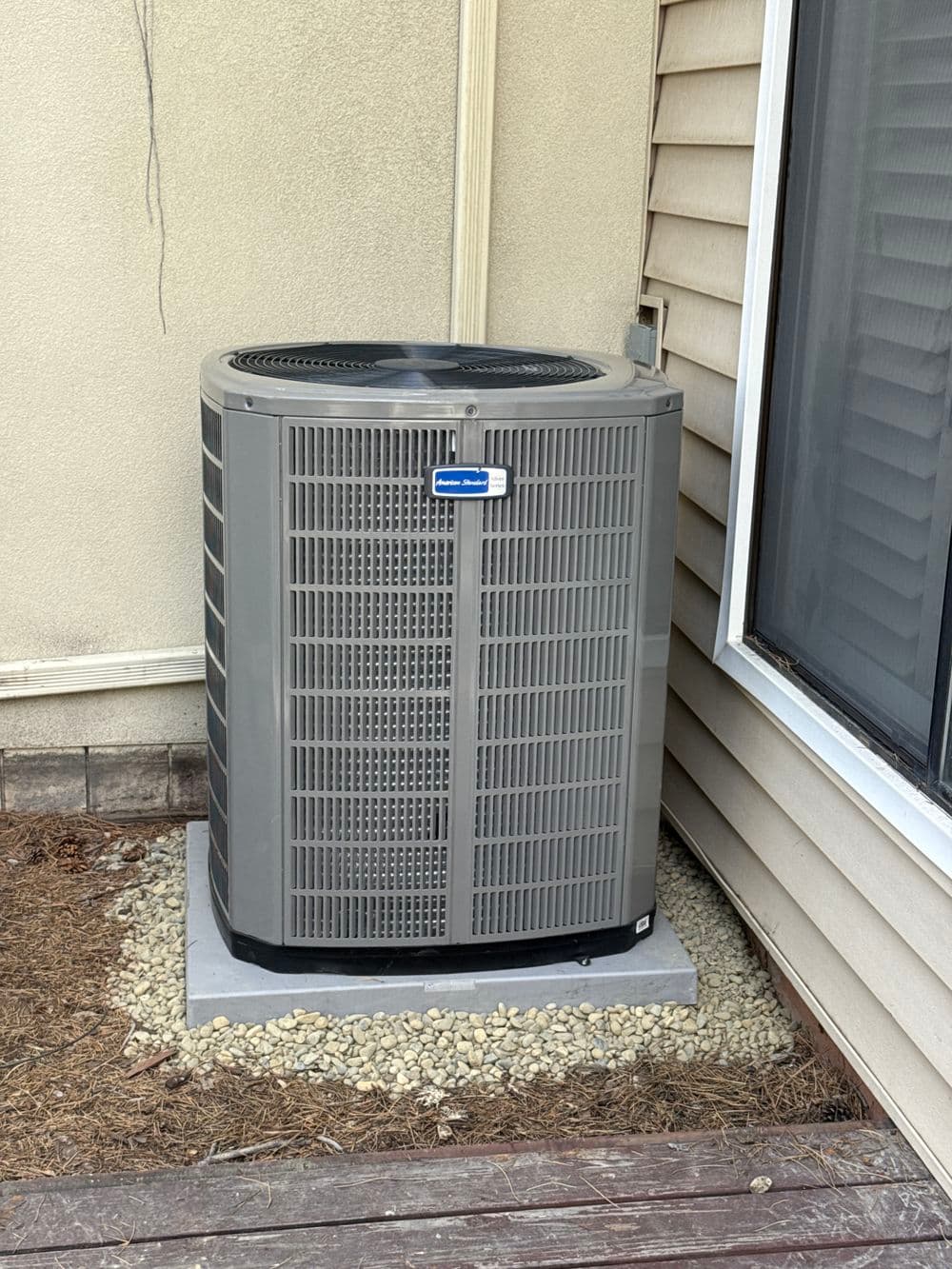 Air conditioning unit on a concrete pad beside a house, featuring a gray exterior and ventilation grille.