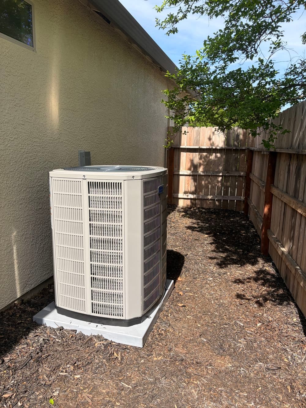 Air conditioning unit installed beside a house in a shaded outdoor area.